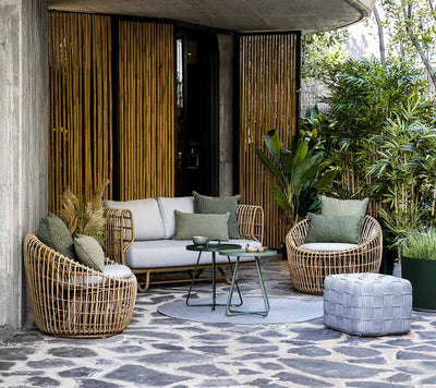 Outdoor furniture set with sofa and armchairs on a slate patio in front of bamboo wall