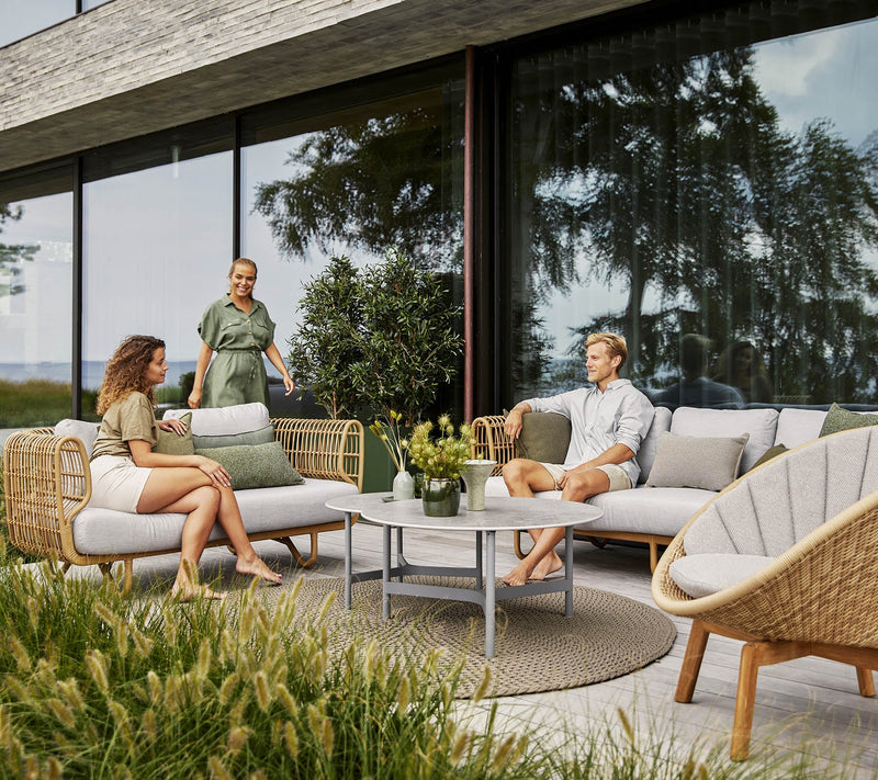 Couple sitting on outdoor furniture with a woman walking towards them