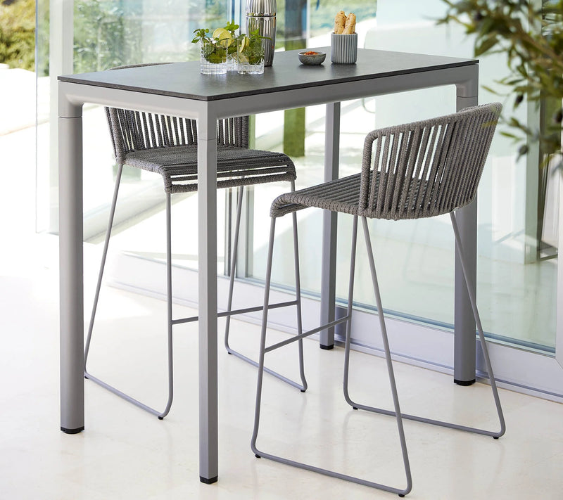 Rectangular bar table with two grey bar chairs against a glass wall