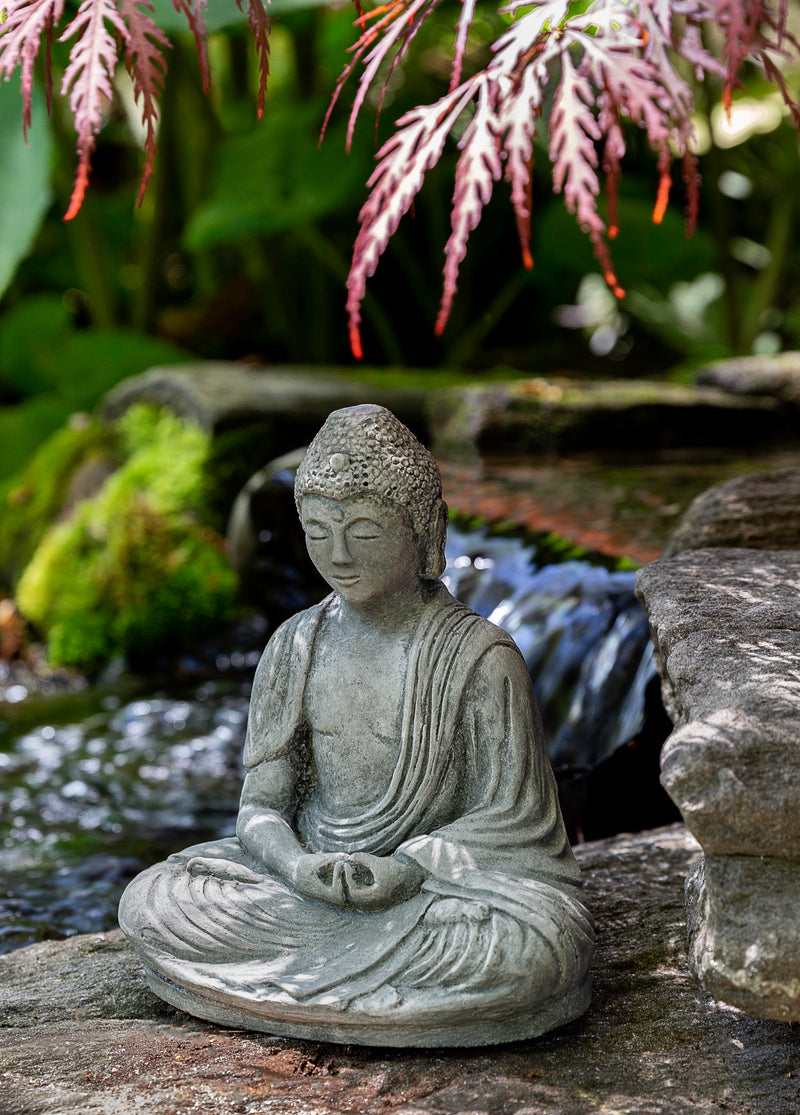 Sitting buddha in front of pond with maple tree branch