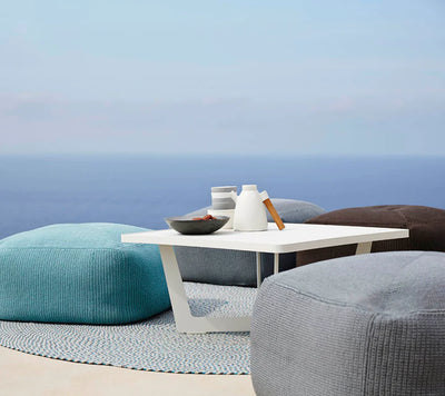 One blue footstool and one gray next to a white coffee table by the ocean