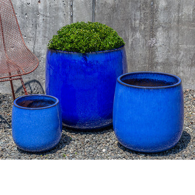 Grouping of 3 blue containers shown in front of concrete wall