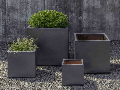 Grouping of 4 grey square containers shown in front of concrete wall