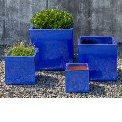 Grouping of 4 square blue containers shown in front of concrete wall
