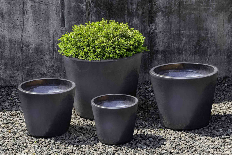 Grouping of 4 grey containers shown in front of concrete wall