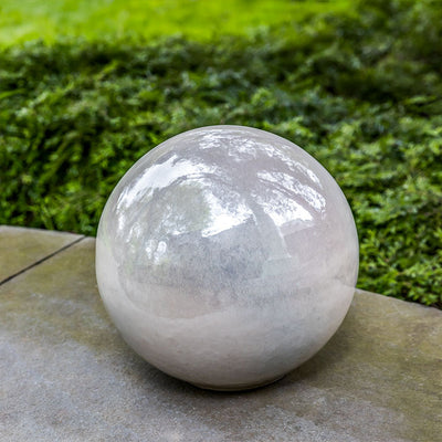 White glazed ceramic sphere displayed in front of greenery