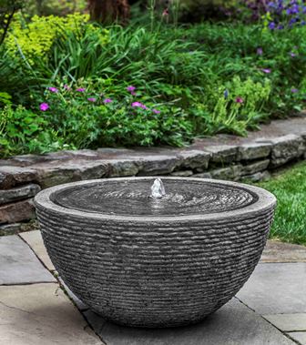 Grey bowl fountain pictured in front of planted hedge
