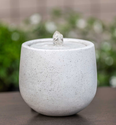 Speckled white table top fountain with water flowing out of copper spout