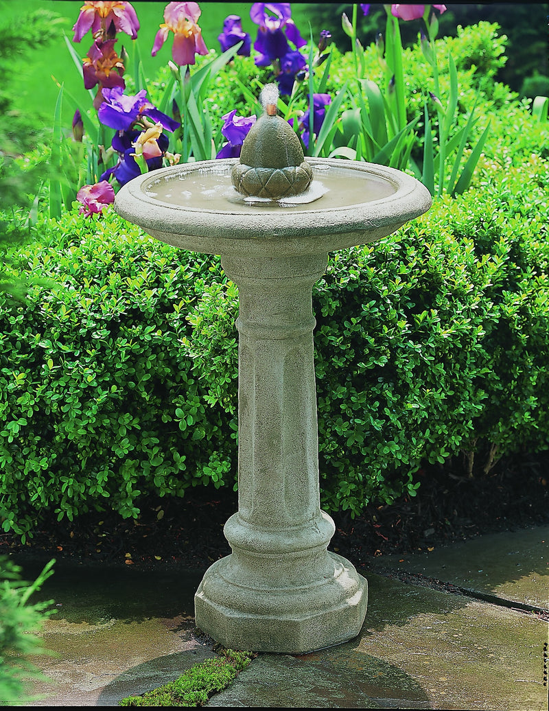 A cast stone outdoor fountain pictured in front of flowering iris.
