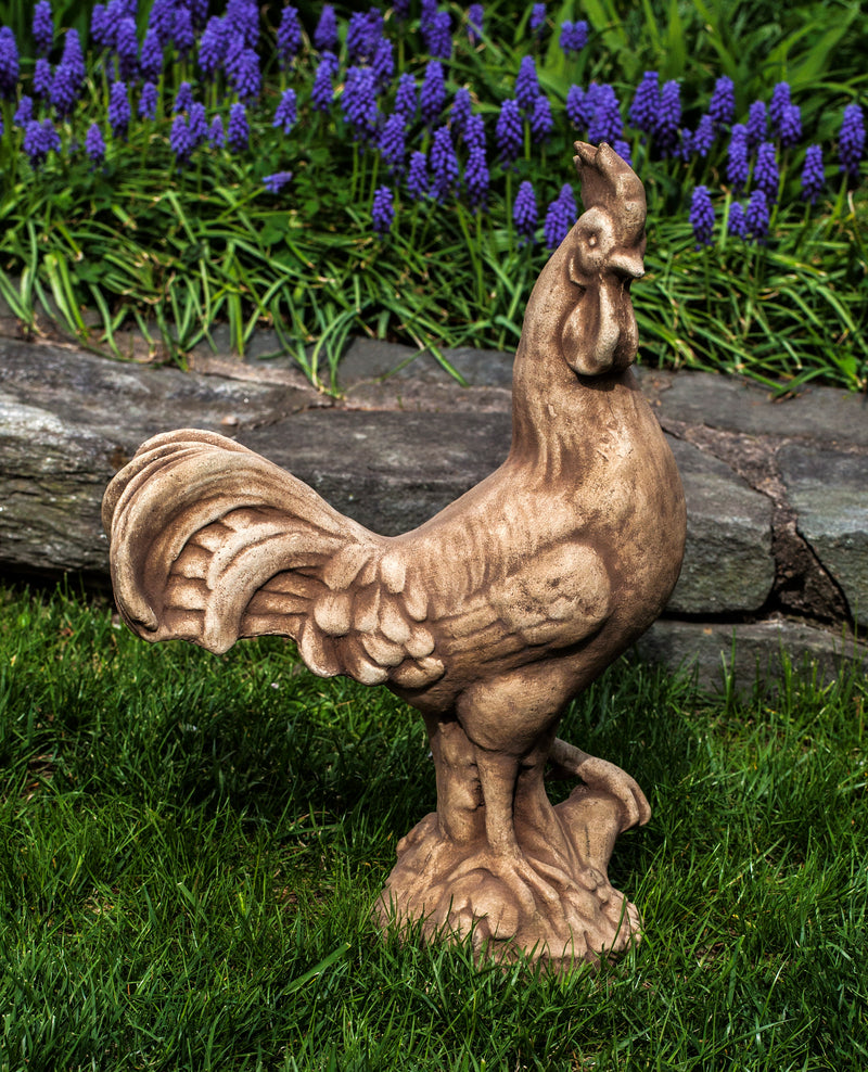 Light brown rooster standing in grass in front of flowers