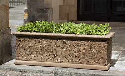 Long window box decorated with simple arabesque designs, planted with green plants