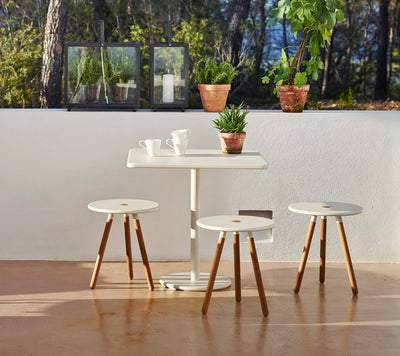 Outdoor square table with three stools in front of white wall