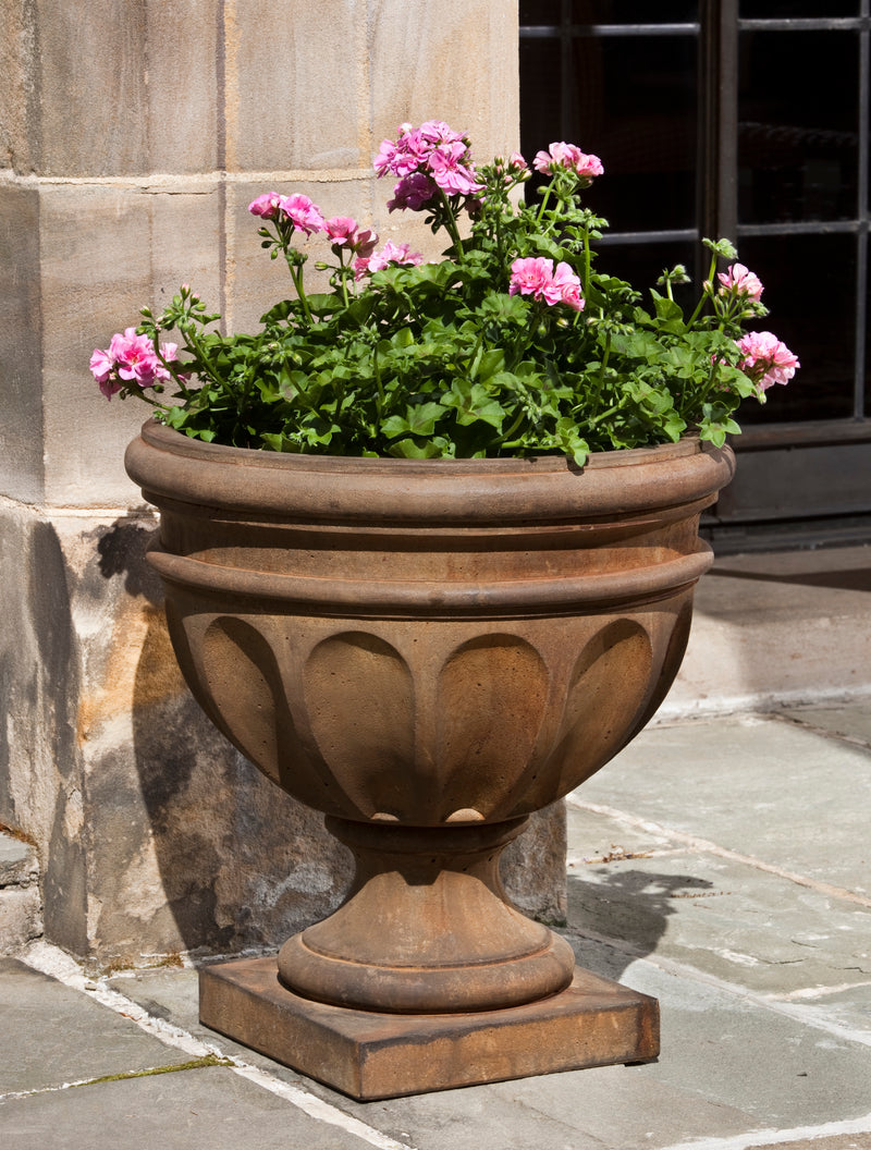 Classic concrete urn with rolled rim and decorated sides, planted with pink geraniums