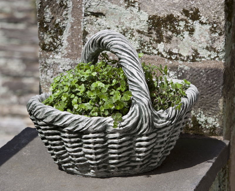 Basket shaped container planted with perennials in front of stone wall