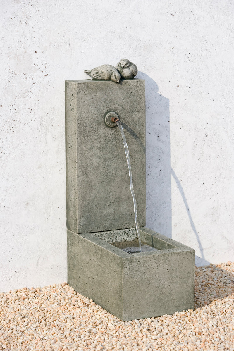 Small wall fountain with rectangular top and basin with a single spout, a pair of birds perched on top