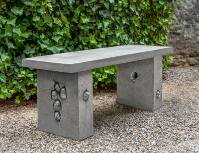 Grey, cast stone bench with design of birds peeping out of holes on the side of the legs
