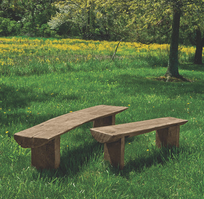 Two benches made to look like they are carved from wooden logs, pictured in a meadow of yellow flowers