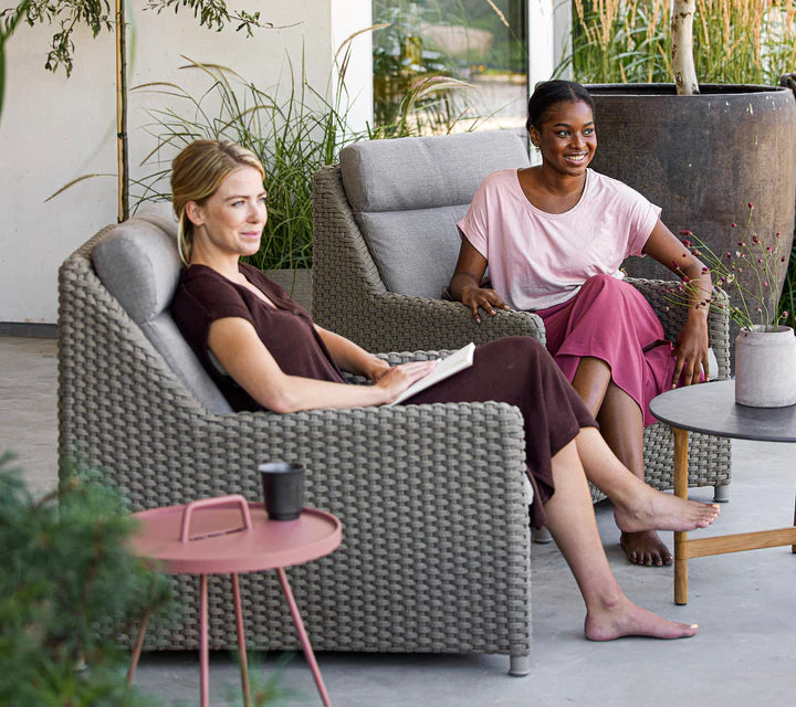Two women sitting on matching highback chairs next to rose colored coffee table