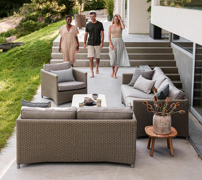 Three people walking toward outdoor sofas  and armchair by a lawn