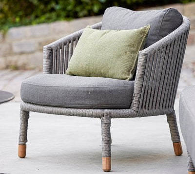 Gray woven outdoor armchair with matching cushions and a green throw pillow