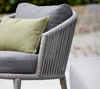 Close up of a gray woven outdoor armchair with matching cushions and green throw pillow
