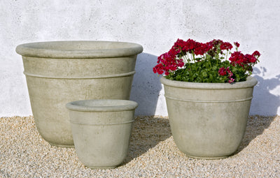 Trio of grey containers pictured in front of white wall, one planted with red geraniums