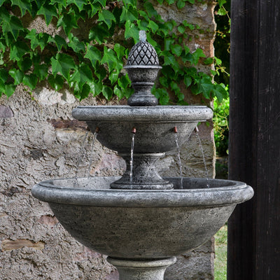 Close up of two-tired fountain with pineapple finial and water spilling into large bowl through copper tubes