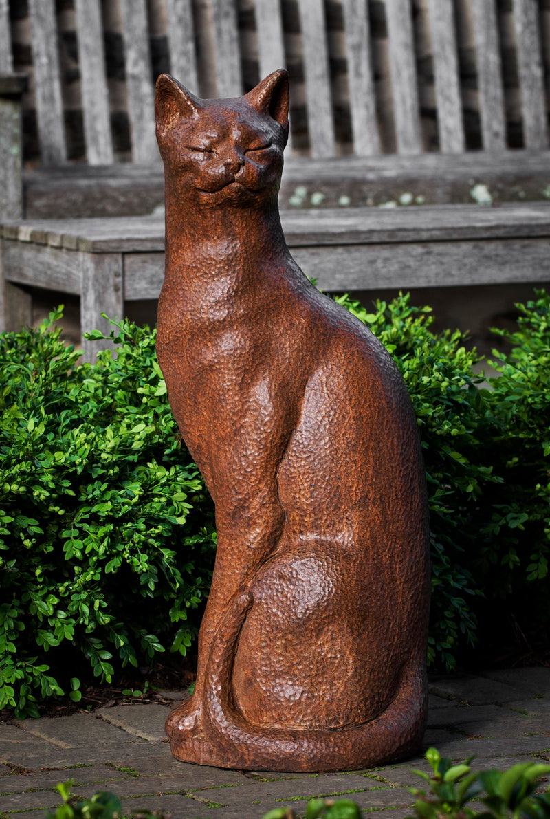 Brown cat sitting tall in front of boxwood
