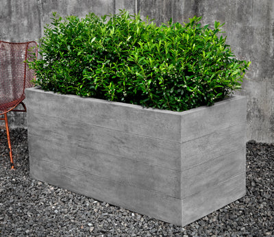 Rectangular cast stone container shown planted with shrubs and next to a metal chair