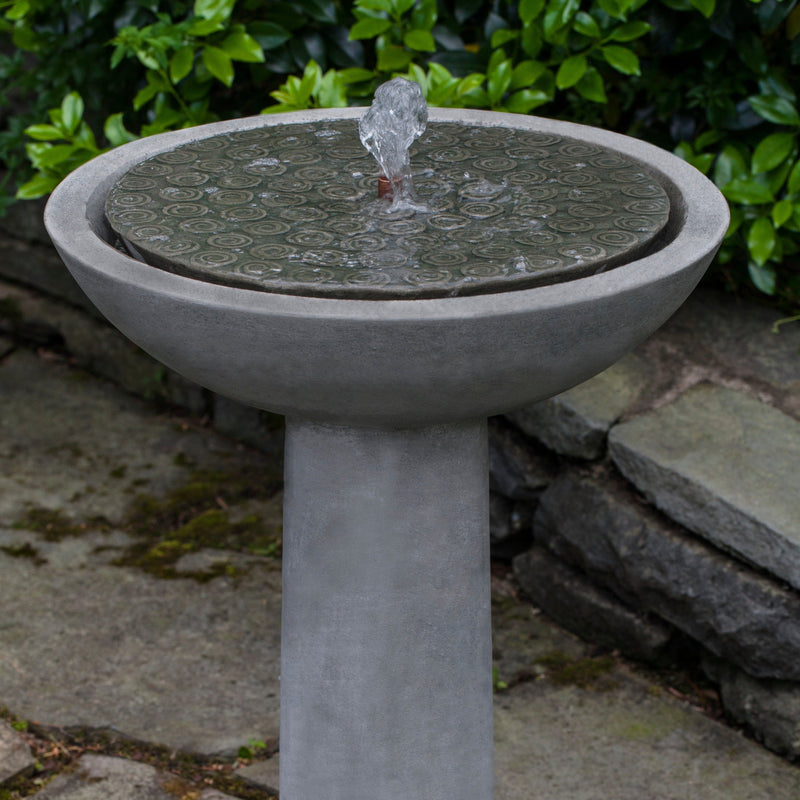 Birdbath fountain with covered bowl and copper spout on top of round pedestal