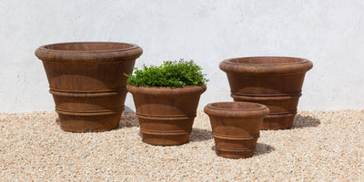 Grouping of 4 cast stone containers  in different sizes shown in front of light grey wall and gravel