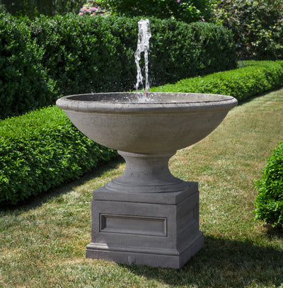 Large bowl with tall water flow on top of square pedestal pictured on grass