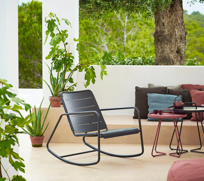 Contemporary black rocking chair on white terrace surrounded by potted plants and coffee tables
