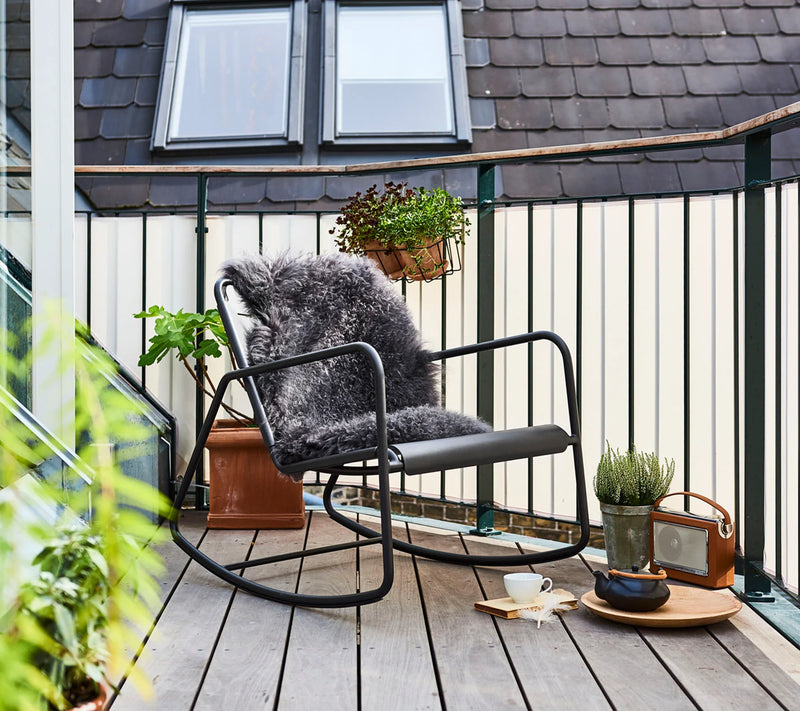 Contemporary black rocking chair with fir throw sitting on wooden deck next to coffee tray