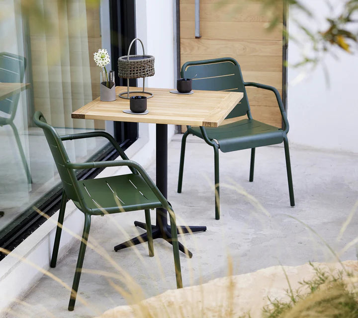 Bistro set with teak table and two metal chairs shown in front of large window