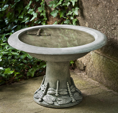 Small round birdbath with one dragonfly inside bowl and at the bottom of the stand