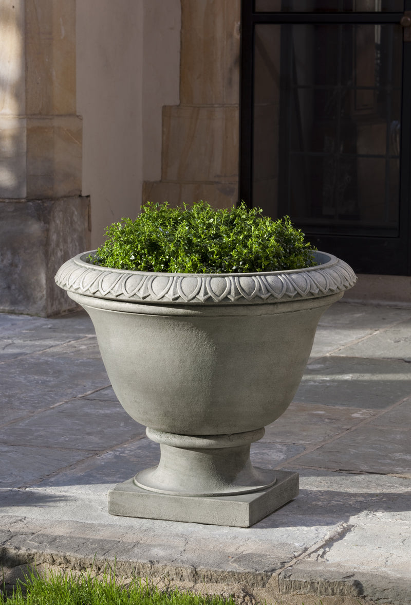 Classic light grey urn planted with a shrub and shown on stone patio