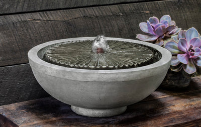 Low round table top fountain with etched covered top pictured on wooden bench next to succulents