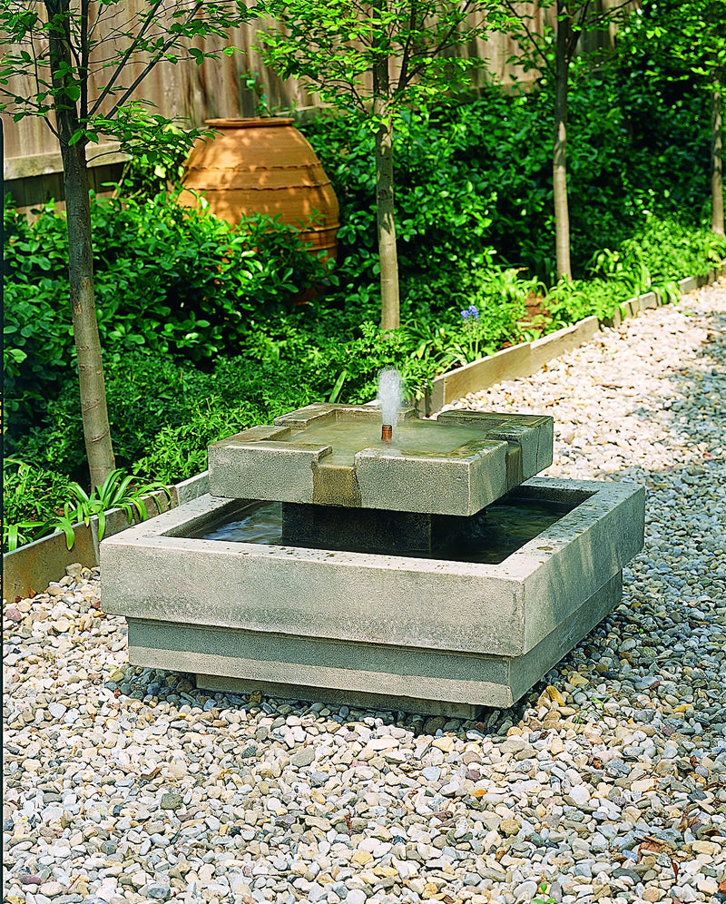 Square two tiered fountain pictured on gravel by a perennial bed