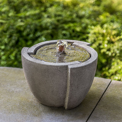 Small tabletop fountain with bubbly spout pictured in front of greenery