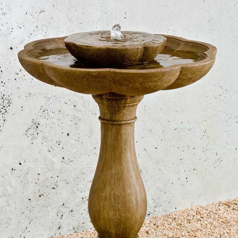 Detail of light brown fountain with flower shaped bowls pictured in front of white wall
