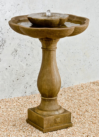 Two flower-shaped bowls on top of curvy pedestal and square plinth pictured  on gravel ground