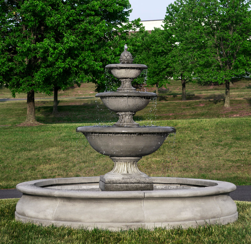 Three tiered estate fountain in round basin pictured on grass in front of large trees