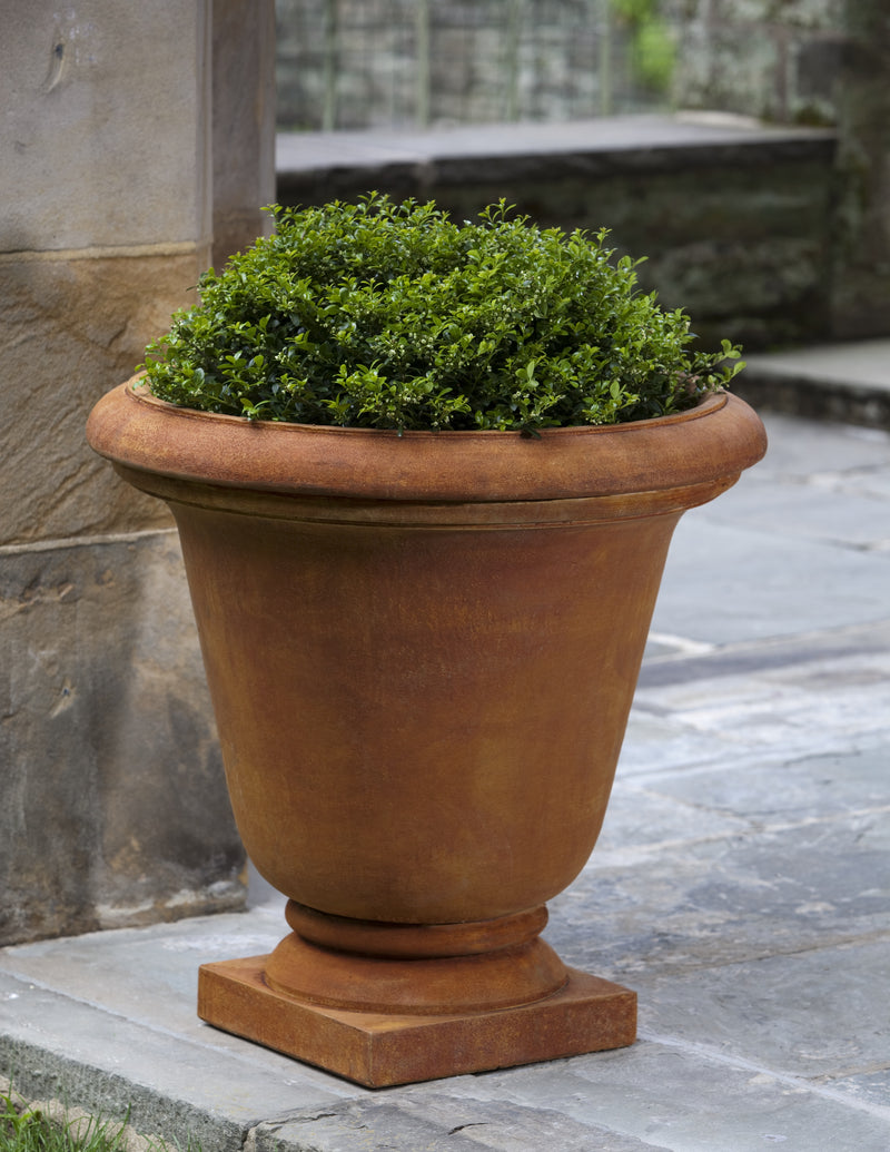 Tall urn in reddish tones planted with a shrub and shown on stone terrace