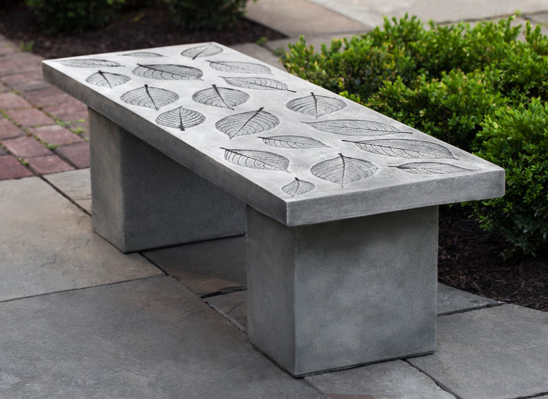 A grey cast stone bench with a design of pressed hydrangea leaves on the top