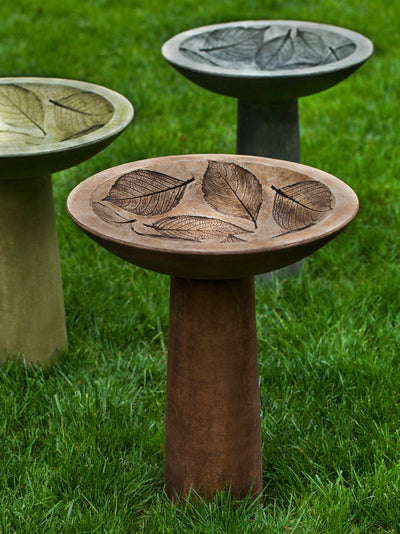 Three birdbaths in brown, green and black with hydrangea leaves etched in bowls, standing in lawn