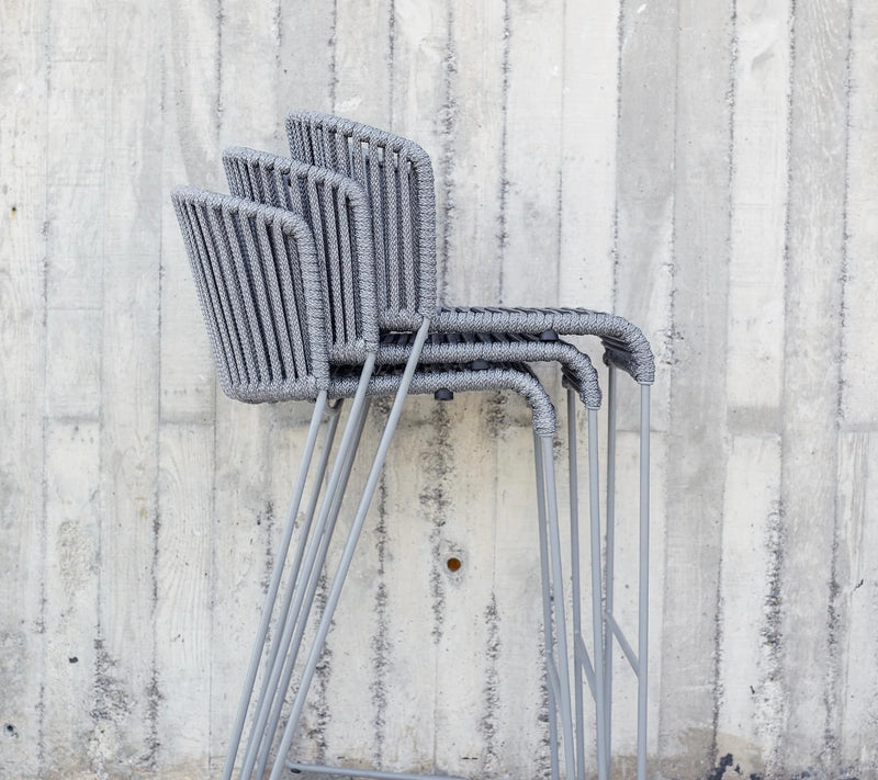 Three stacked bar chairs in front of grey wall