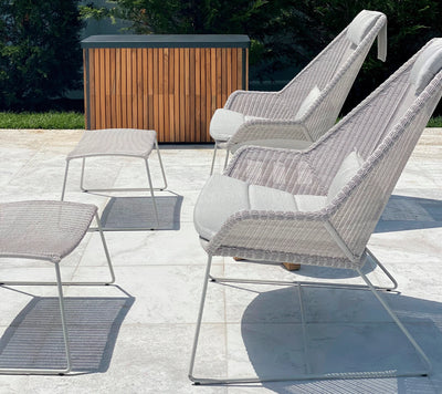 Two light gray armchairs with matching footstools on patio