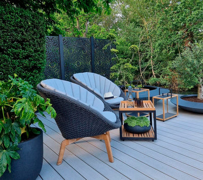 Armchair set with coffee tables on gray decking and lush garden in the background