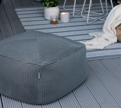 Gray footstool on light gray terrace next to a throw blanket